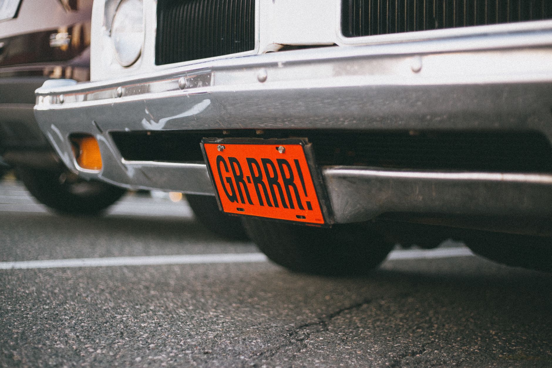 Close up of a vintage car with a custom orange license plate reading 'GR RRR!' in a parking lot.