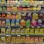 Variety of snacks in an indoor supermarket aisle, colorful packaging.