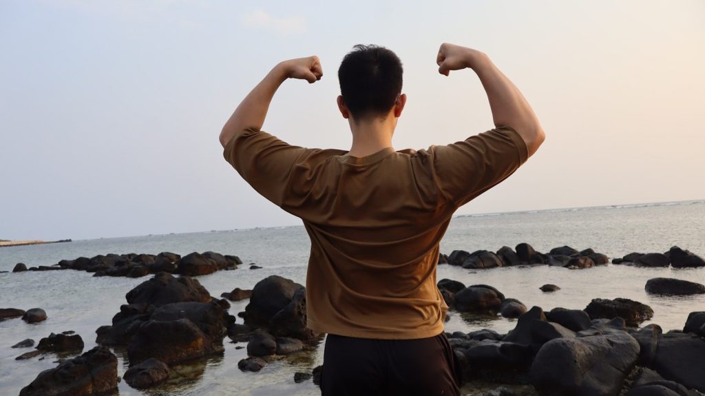 Man flexing muscles by the rocky ocean shore