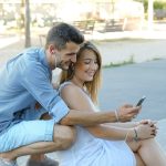 a man and a woman sitting on a bench looking at a cell phone