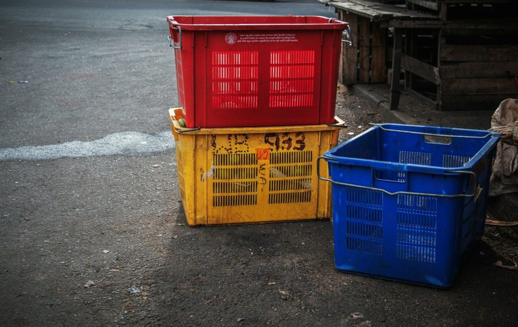 Three colorful plastic crates stacked on pavement.