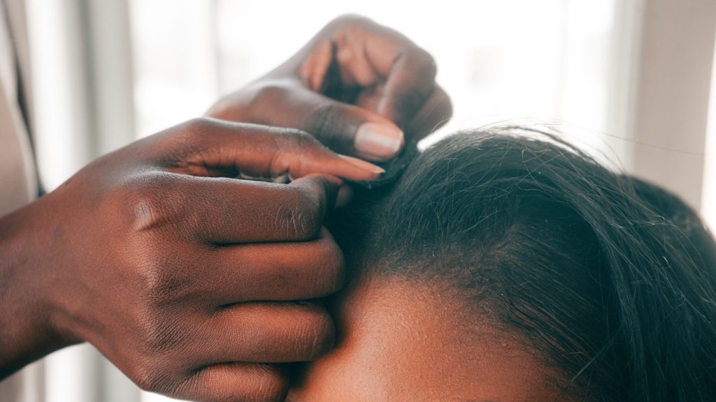 Dark hands braiding dark hair.