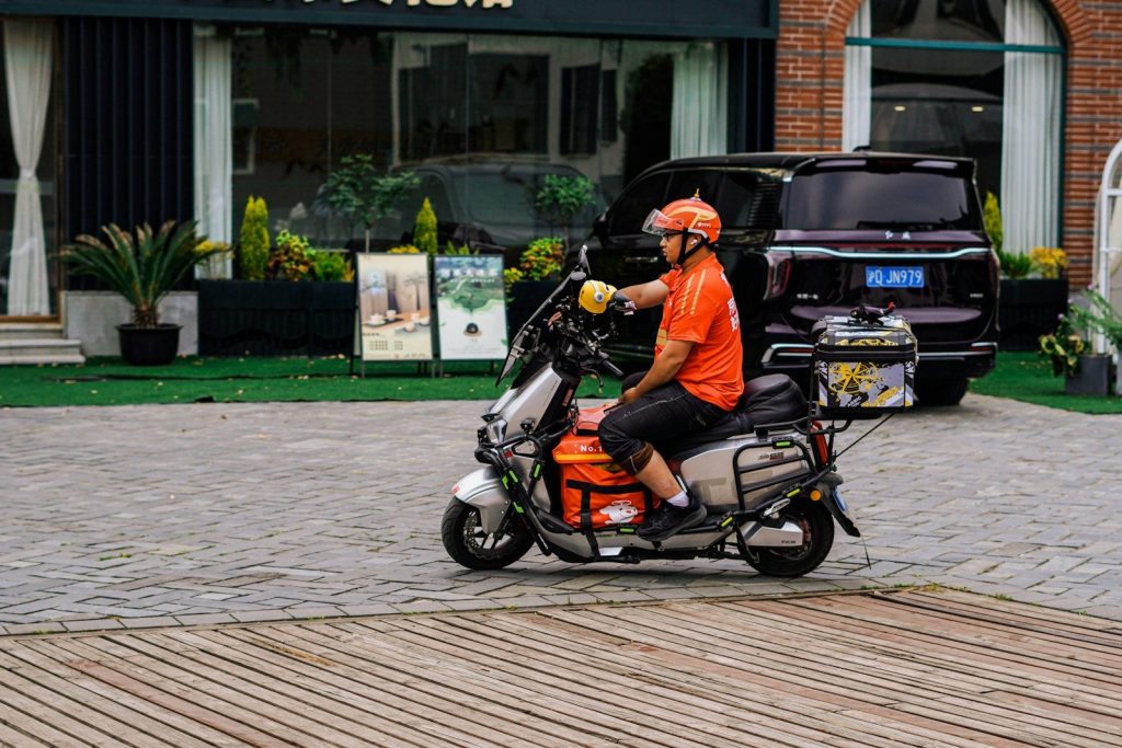 Man in orange helmet riding a delivery scooter.