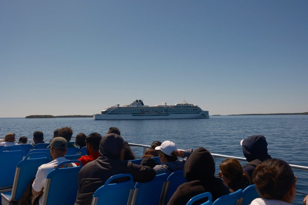 Boat passengers observe a large ship under a clear sky.