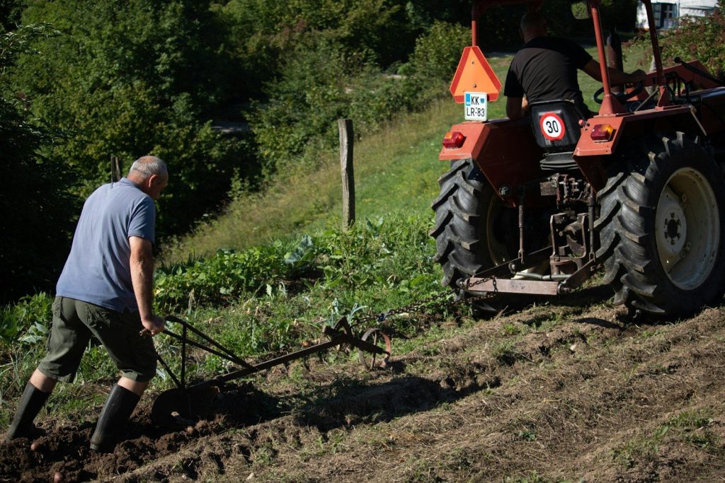 Man plowing field with tractor on grassy slope.