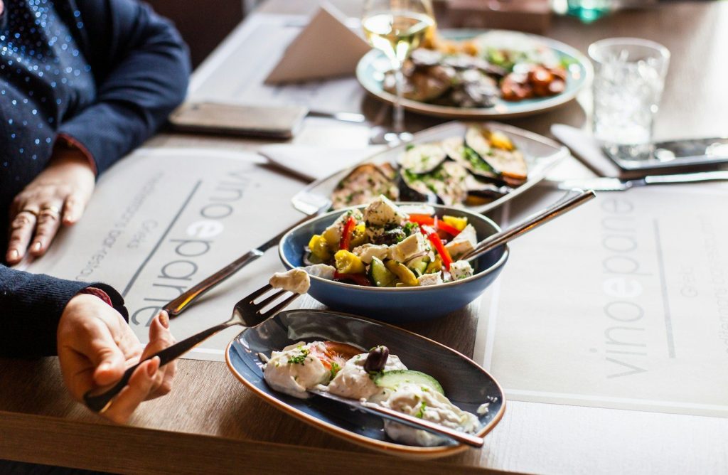 person holding chopsticks in front of vegetable salad on black ceramic bowl