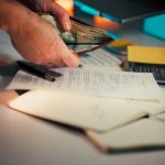 Hands holding cash over desk with papers.