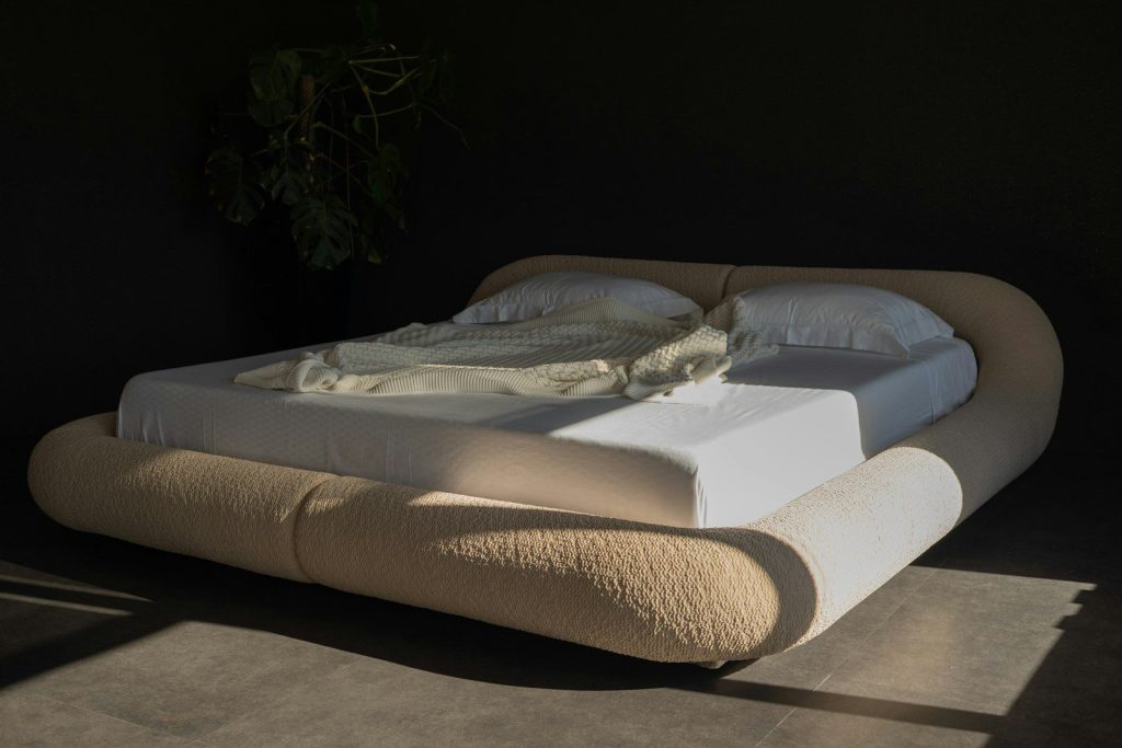 Modern bed with rounded headboard and white linens.