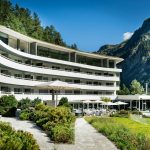 white concrete building near green trees and mountain during daytime