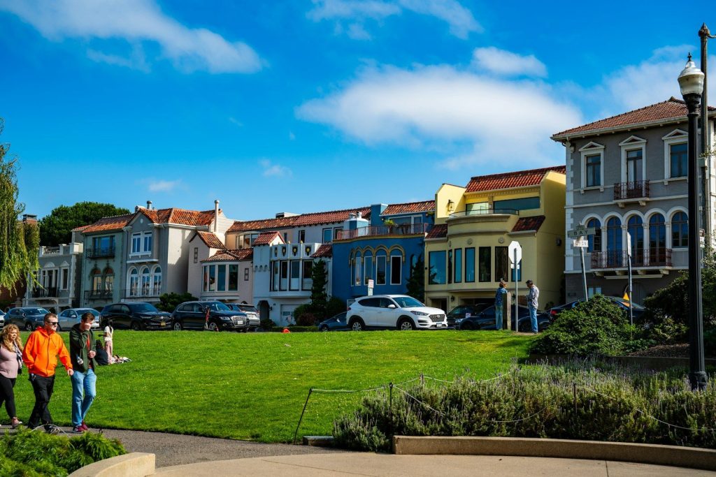 Colorful houses line a street with people walking on grass.
