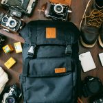 high-angle photo of black bag beside cameras, portable HDD and black leather lace-up boots