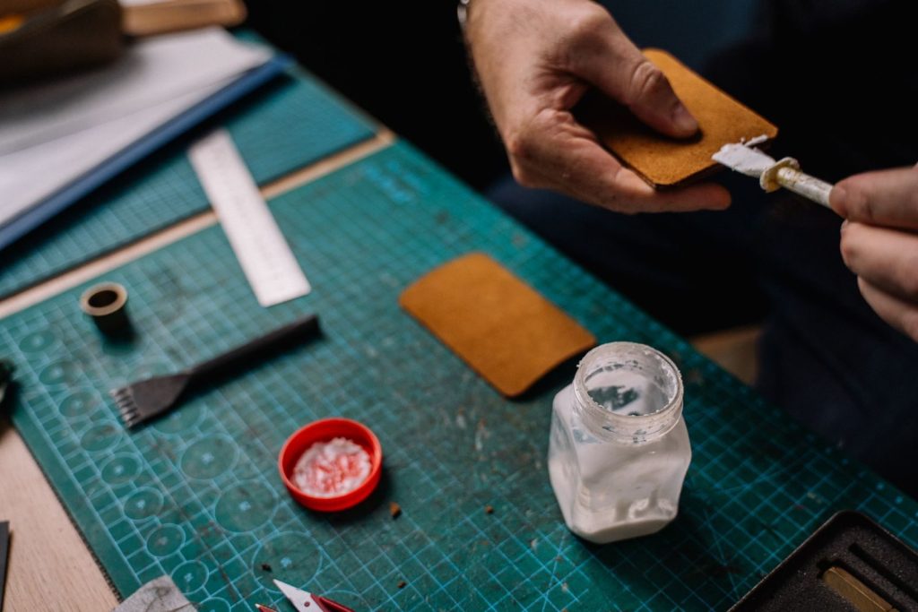 A detailed close-up of a person applying glue on leather for crafting purposes, showcasing handwork and tools.