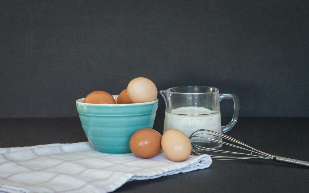 a bowl of eggs next to a glass of milk