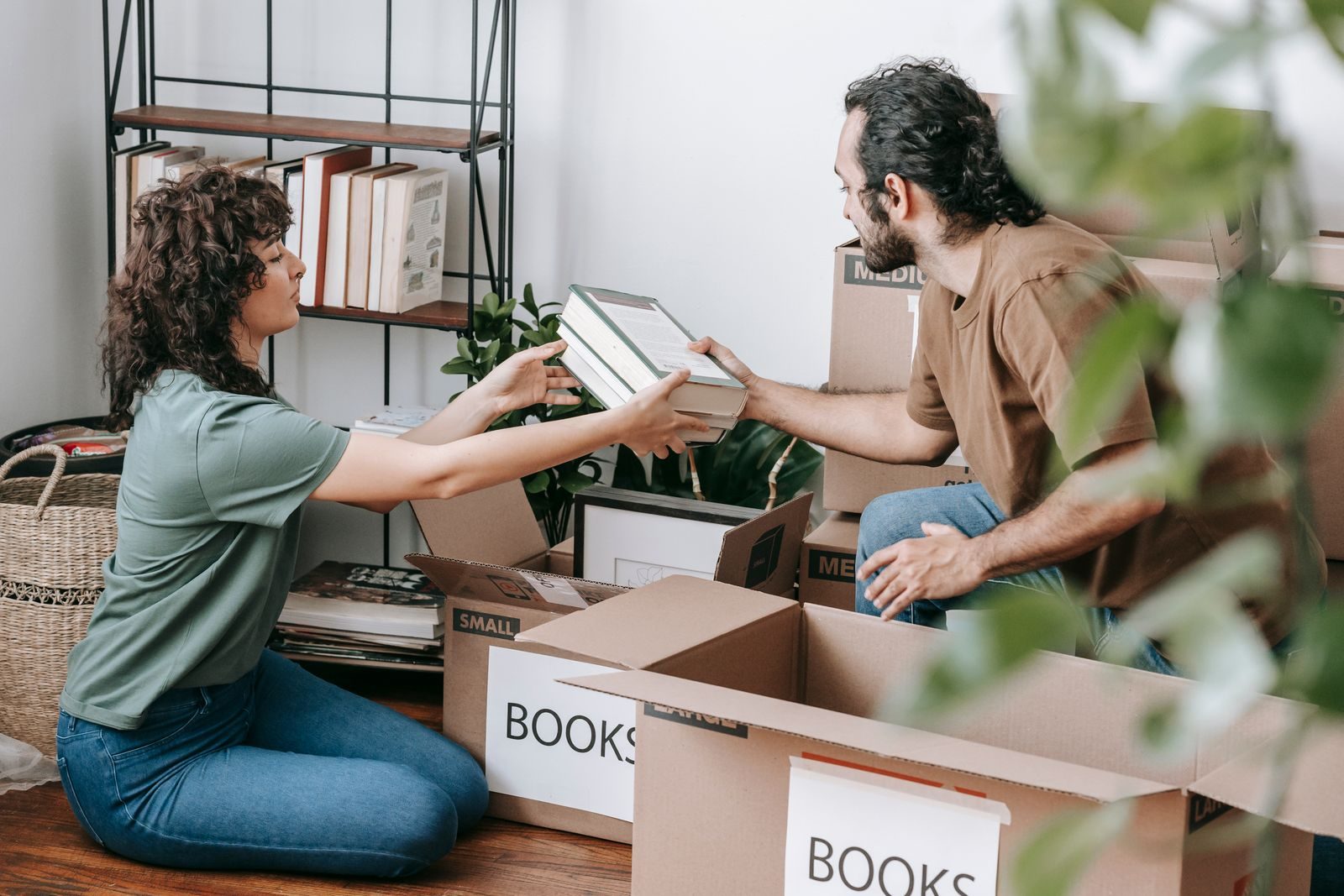 A couple organizing and packing books in cardboard boxes indoors, preparing for a move.