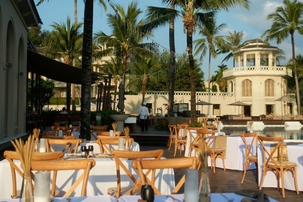 Outdoor dining area with tables set under palm trees.
