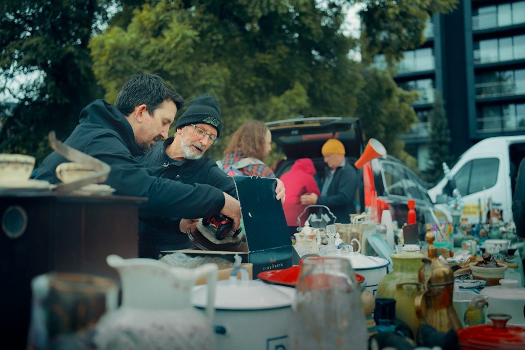 Men browsing items at an outdoor market stall.
