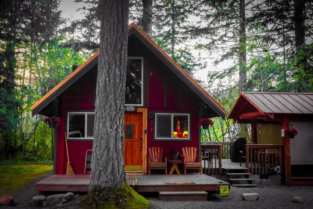 A red cabin nestled among trees with a small shed.