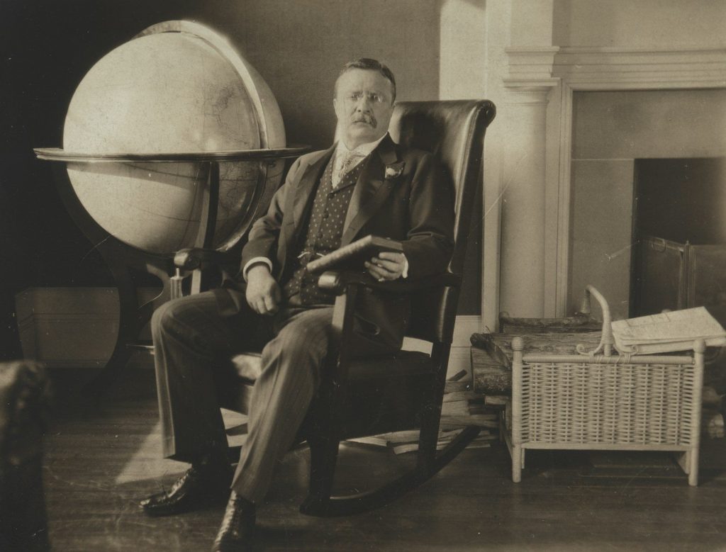 Man in rocking chair beside globe and fireplace.