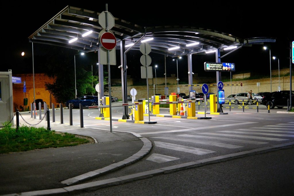 Illuminated parking entrance with barriers and signs at night.