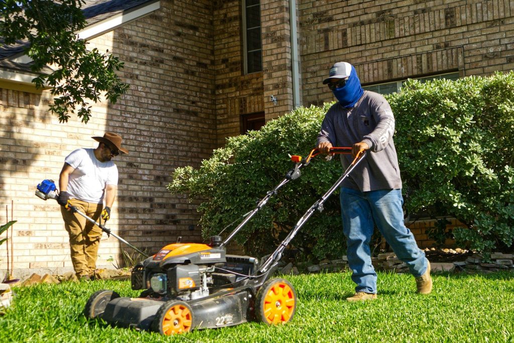 Two men mowing and trimming a residential lawn.