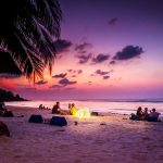 people sitting near seashore viewing sea under orange and blue skies