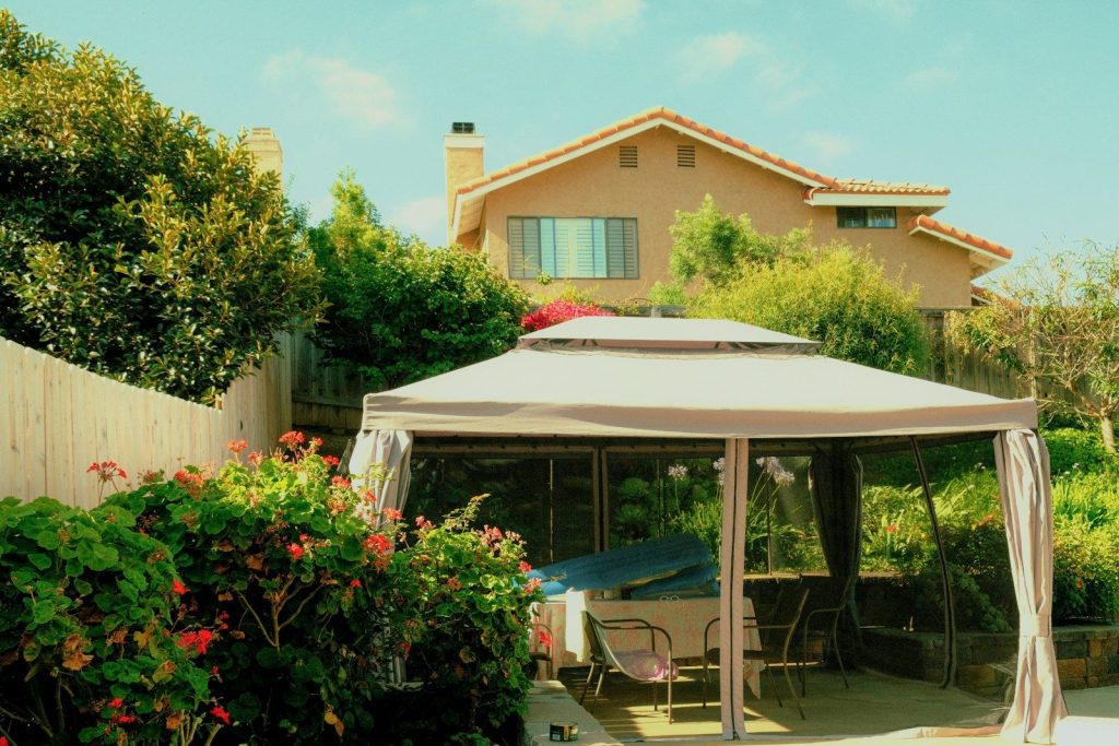 A backyard gazebo with a house and lush greenery.