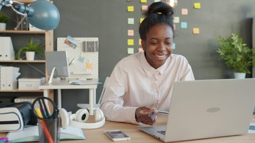 Woman smiling while working on a laptop at a desk.