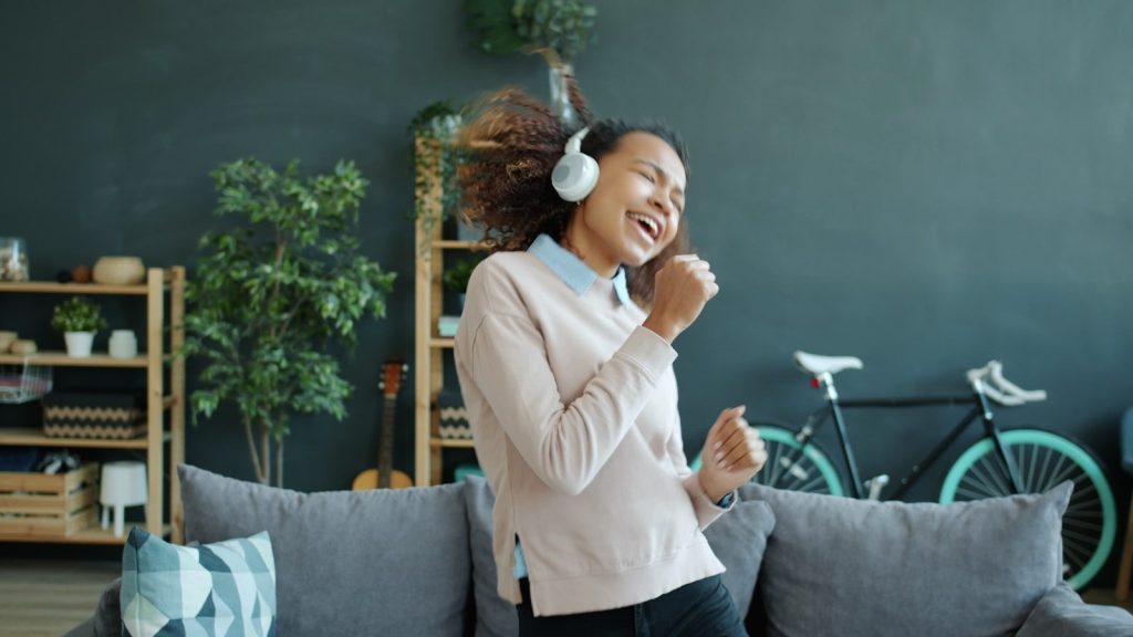 A woman with headphones singing and dancing joyfully.
