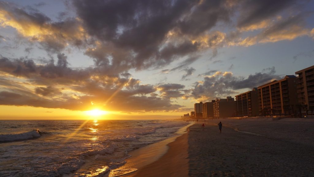 the sun is setting on the beach near a hotel