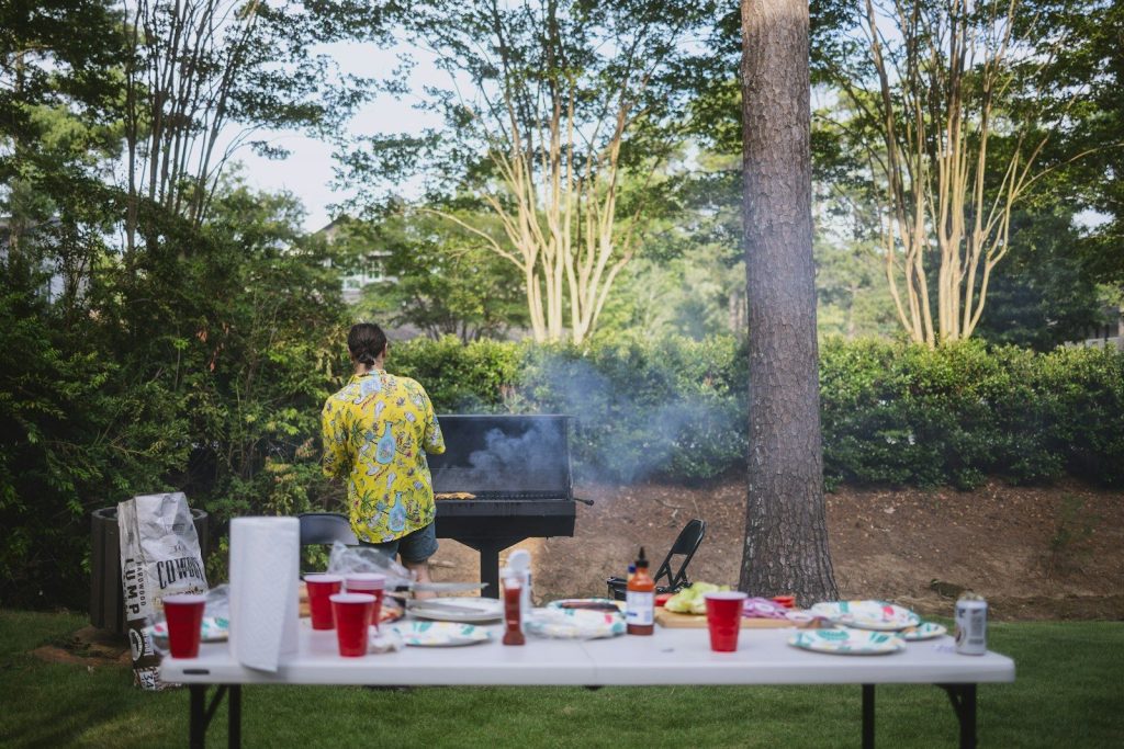 Person grilling outdoors with a table of food and drinks.