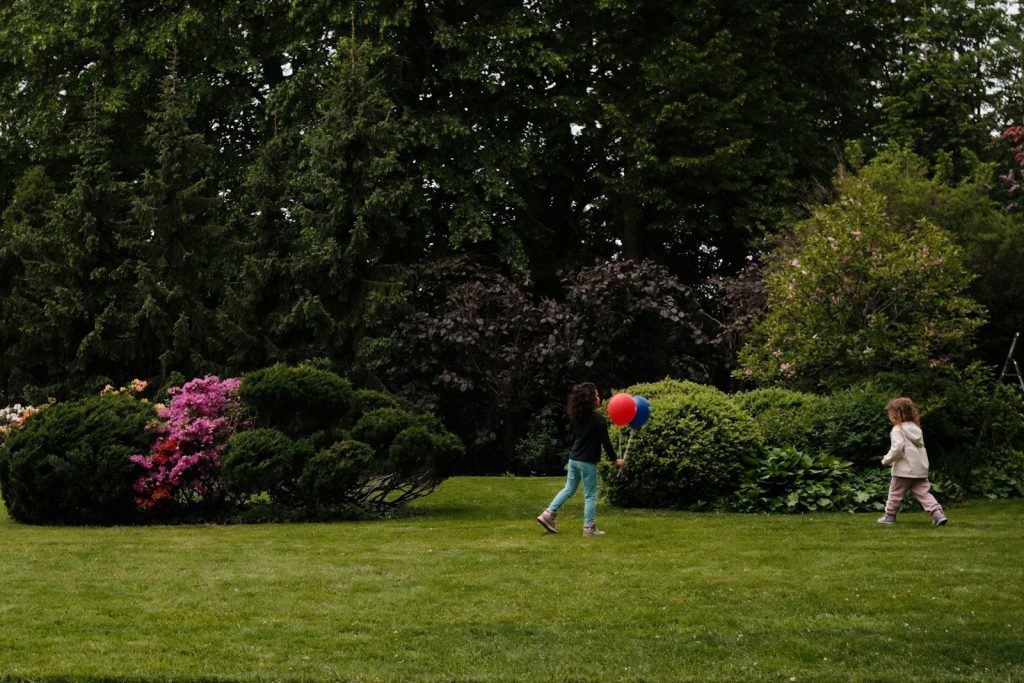 Two children playing with a balloon on a green lawn.