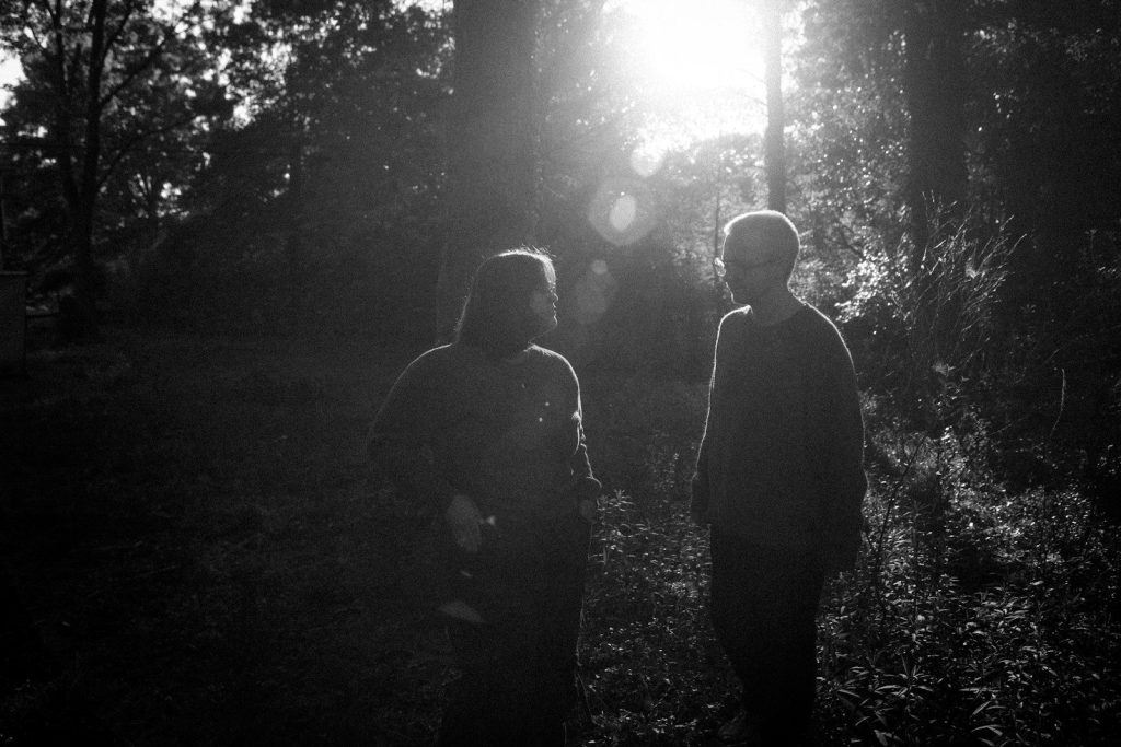 Two people silhouetted in a sunlit forest.