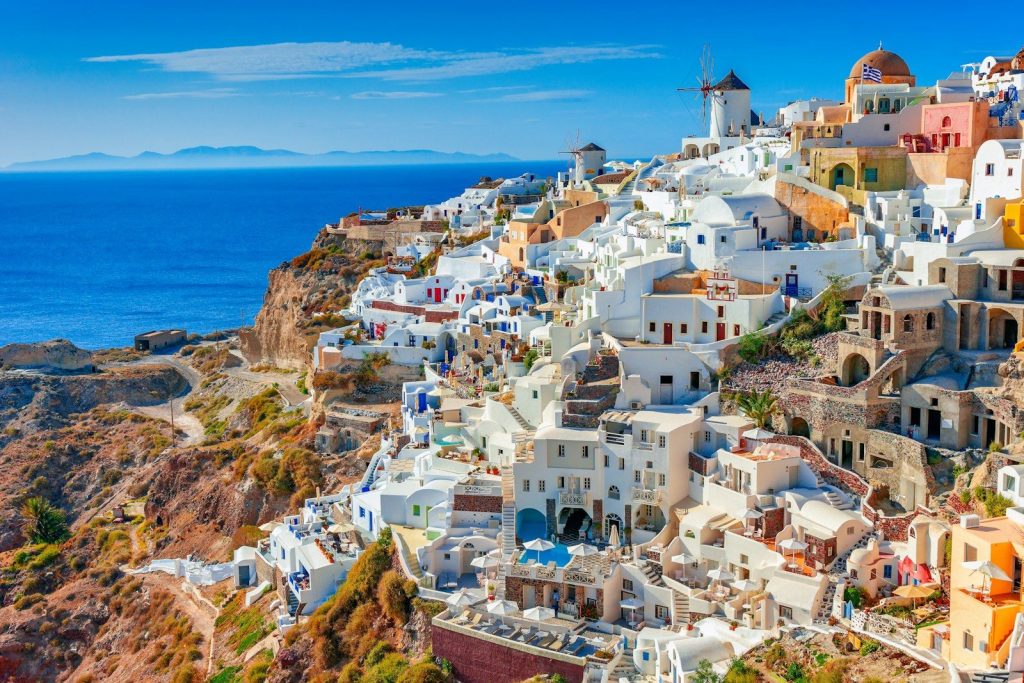 White village on a cliff overlooking the blue aegean sea.