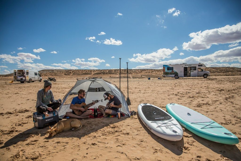man in black t-shirt sitting on brown sand near white tent during daytime