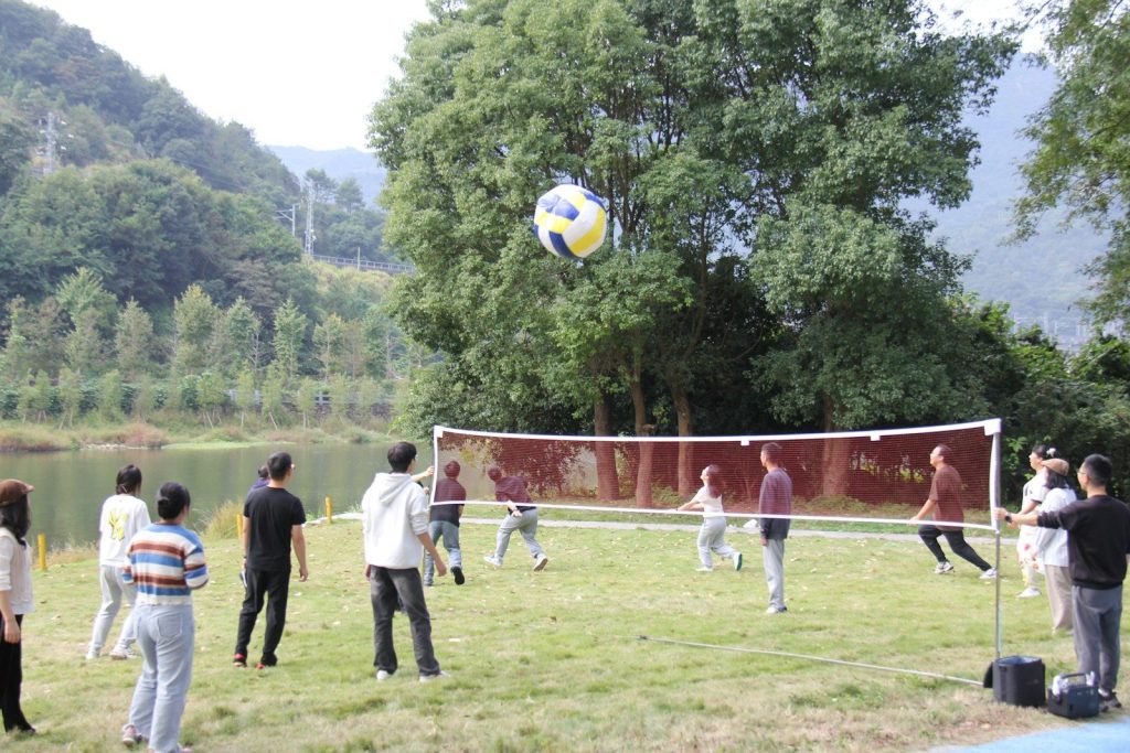 People playing volleyball outdoors by a lake.