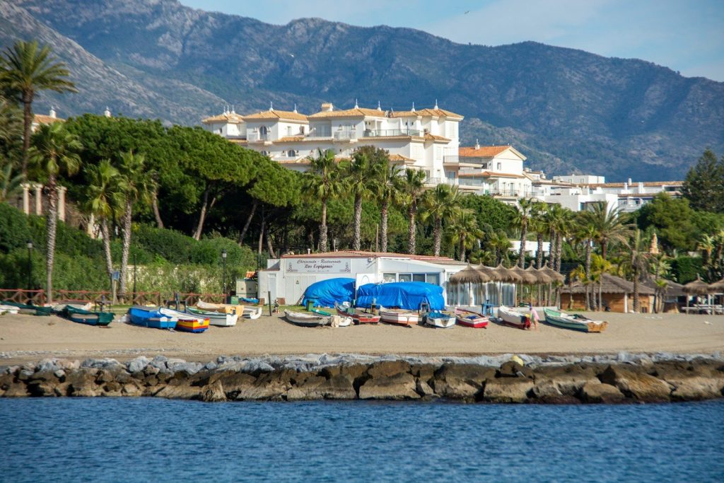 Small boats on a beach with buildings and mountains.