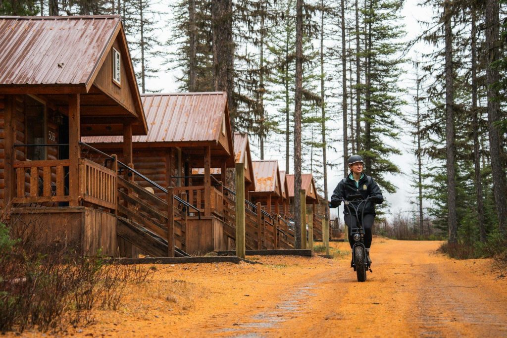 Person riding electric scooter past cabins in forest.
