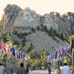 a group of people walking on a path with flags and Mount Rushmore National Memorial in the background