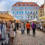 A street market bustles with people and clothing stalls.