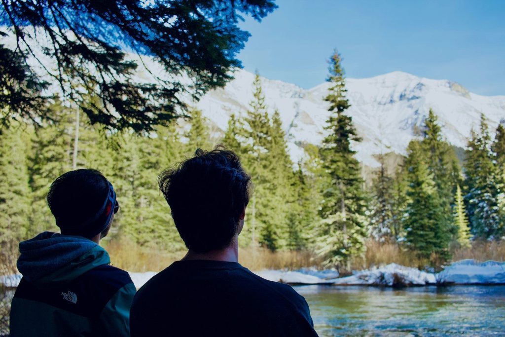 Two people look at snow-covered mountains and forest.