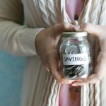 a woman holding a jar with savings written on it